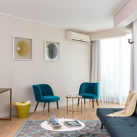 ليوناردو كلوب هوتيل البحر الميت - شامل كلياً نيفيه زوهار المظهر الخارجي الصورة The photo depicts a modern living room setting. The room features a dark blue sofa with a light throw blanket draped over it. There are two stylish teal accent chairs positioned around a small round coffee table, which holds various items. A flat-scr